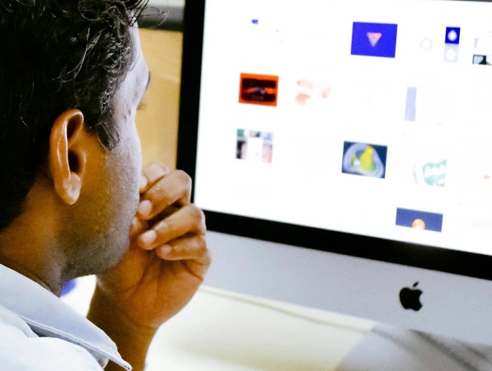 man sitting in front of silver Apple iMac on table